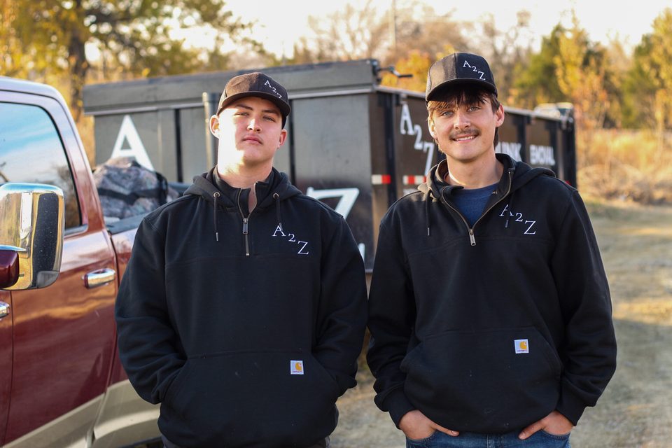 Luke Hook and Fin Kimura, owners of A2Z Junk Removal, standing in front of their trailer in Broken Arrow, Oklahoma
